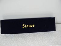 Navy blue velvet box with gold Stauer logo on top, showing the packaging of the bracelet.