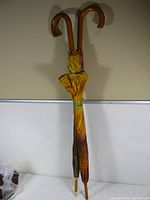 Full view of two umbrellas side by side showing wooden curved handles and fabric featuring sunflower and cat prints.