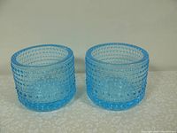 Pair of blue glass bowls with hobnail texture, shown side by side on light patterned surface.
