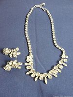 Full view of Sherman necklace and matching rhinestone earrings on blue fabric background.