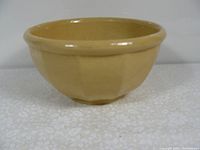 Side angle view of a beige ceramic bowl with a smooth rounded rim and textured vertical indentations on the exterior.