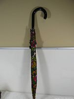 Full view of closed umbrella standing upright showing black curved handle and floral patterned fabric cover.