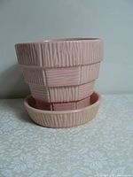 Pink ceramic plant pot with wood grain texture and matching saucer shown from side angle.