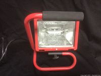 Front view of red framed Ace work light with clear protective glass and bulb inside, placed on black background.