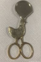 Top view of the egg cutter features round metal blade and detailed rooster body attached to scissors-like handles.
