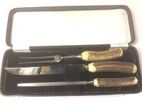 Three-piece Atkinson Sheffield carving set in black velvet-lined case with white satin lining, featuring fork, carving knife, and sharpening steel with antler handles.