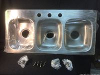 Triple stainless steel sink with three basins, protected partially with plastic wrapping for one basin. Sink is rectangular and bar-sized.
