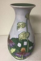 Front view of the Benaya vase showing raised floral and leaf pattern in green, purple, white, and yellow on a pale background.