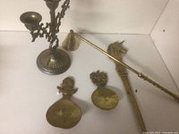 Overall view of four brass items showing a candelabra, two spoons with ornate handles, and a horn-shaped item on white background.