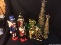 Photo of three nutcracker figurines in traditional colors and two gold wire Christmas trees with star toppers.