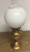 Electrified copper lantern with white glass globe shade on top, copper base with pedestal design, viewed at close range against plain background.