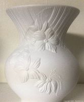 Image of the white ceramic vase showing the embossed floral detail and bulbous shape.