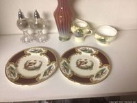 Photo displaying two decorative china plates with rooster motifs, a gradient ribbed glass vase, a set of clear glass salt and pepper shakers on a tray, and a floral-themed creamer and sugar bowl.