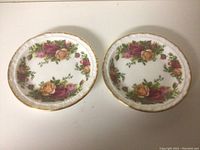 Two small dessert plates with floral rose decoration and gold trim, topside view.