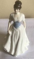 Front view of the porcelain figurine showing woman in white gown with blue corset detail and brown updo hair.