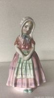 Front view of the Royal Doulton Tootie figurine showing the girl in bonnet with checkered apron and pink dress.