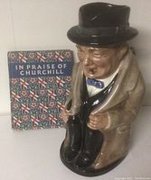 Front view of the Royal Doulton Winston Churchill Toby Jug next to the book.