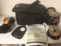Ryobi MultiTasker leveller device, black with orange details, carrying case, several leveling heads, and printed manuals laid out on a flat surface, showing all included parts.