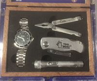 Photo of the gift set in wooden box displaying watch, pliers multi-tool, folding utility knife, and flashlight.
