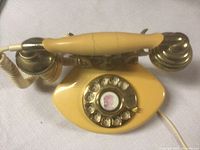 Front top view of yellow vintage rotary dial telephone displaying rotary dial and metallic handset with coiled cord