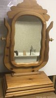 Front view of wooden vanity mirror showing mirror and base with hinged lid closed