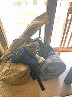Camping gear piled near door; visible sleeping bags, tent, lantern, backpacks