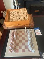 Chess set with carved light and dark wooden pieces arranged on a beige and reddish checkered chessboard, wooden backgammon board closed behind it, and tilt maze game on top of backgammon board.