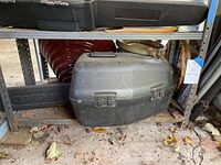 Closed black hard plastic carrying case on a metal shelf outdoors, containing a Craftsman chainsaw inside.