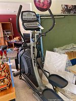 Full side view of the elliptical machine showing the footing, pedals, handlebars, and control panel.