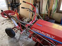 Side view of red Gravely walk-behind mower with seat, handles and front wheel, stored in garage