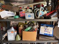 Photo of entire shelving unit with Homelite chainsaw on top shelf along with various oil containers, tools, and maintenance items.