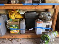 Photo showing black plastic planter, various motor oil containers, WaterAce utility pump box, Spectracide Bug Stop insecticide, and kitty litter bag stored under a wooden bench.