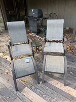 Two adjustable outdoor chairs with matching ottomans and a small side table on a wooden deck with fallen leaves.
