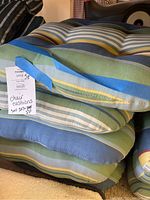 Stack of outdoor chair cushions showing multicolored stripe fabric with blue fastening ties and a lot tag indicating set of 9 cushions.