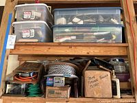 Shelf displaying plastic bins filled with various painting tools and supplies alongside extension cords, coiled wire, and cardboard boxes.