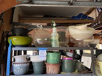 Shelf with multiple planters and a spray bottle including ceramic, glass and plastic varieties.