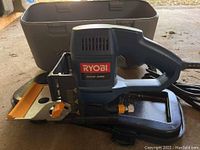 Ryobi biscuit joiner shown outside of orange and gray carrying case on concrete surface.