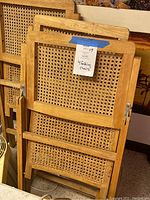 Four folded chairs stacked together showing caned seats and backs with light wood frames.