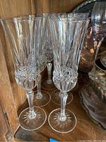 10 clear crystal champagne flutes with vertical cut pattern grouped together on wooden shelf