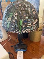 Front view of Tiffany style stained glass lamp with purple and green tones, showing lamp base and electrical cord.
