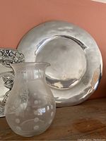 Round heavy metal serving platter, shiny silver tone, placed against a peach-colored wall on a wooden surface.