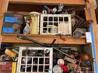 Shelf with plastic organizers filled with assorted screws and nails, zip ties container, and hand tools including a wooden-handled tool and caulk tube.