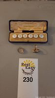 Presentation box open showing six mother-of-pearl shirt studs and two rings on table.