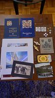 Overview photo showing all items in lot spread on table including books, prints, coins, stamps and souvenir items.