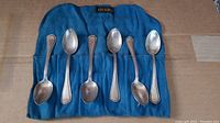Six Birks sterling silver teaspoons arranged on blue fabric pouch labeled Birks.