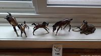 Five ceramic horses displayed on a windowsill in various poses depicting standing, running and lying down.