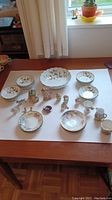 Full overview of assorted china set laid out on table including bowl, bowls, figurines, and pig bank