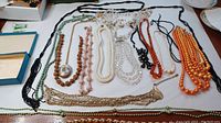 Full assortment showing various necklaces with beads in orange, cream, green, gold, and black colors laid out on a white surface.