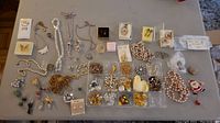 Full overview of various costume jewelry items spread out on a grey surface. Items include necklaces, pins, earrings, bracelets, and brooches arranged for display.