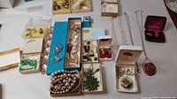 Full overview of the lot laid out on a white surface showing multiple boxes with earrings, necklaces, brooches, and a pearl bead necklace.